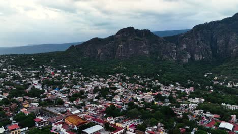 Aerial-view-flying-over-the-town-of-Tepoztlan,-toward-mountains-in-cloudy-Mexico