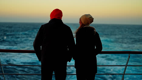 Fun-Couple-In-Warm-Coats-And-Red-Beanie-Hats-Standing-At-Sunset-In-The-Antarctic-Peninsula