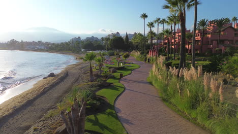 Aerial-view-of-beautiful-Estepona-beach-sunset-walking-path-with-palm-trees-by-the-sea-in-Malaga-Spain,-perfect-family-vacation-holiday-destination,-4K-shot