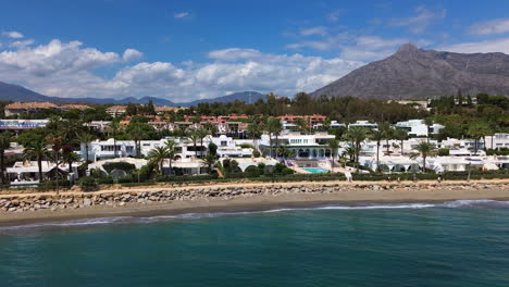 Aerial-view-of-Marbella-beach-and-apartment-houses-with-a-mountain-view,-luxury-vacation-homes-in-Spain,-Malaga-holiday-destination,-4K-shot-moving-right