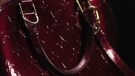 Dark-red-glossy-Louis-Vuitton-handbag-turning-with-black-background,-expensive-luxury-product-made-of-leather,-4K-shot