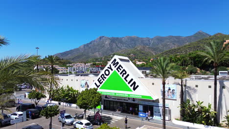 Aerial-view-of-Leroy-Merlin-home-improvement-and-gardening-retailer-with-mountain-view,-big-hardware-store-with-palm-trees-in-Marbella-Malaga-Spain,-4K-shot
