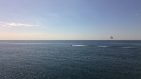 Luftaufnahme-Von-Parasailing-In-Marbella-Malaga,-Lustige-Wasseraktivität,-Schnelles-Boot,-Das-Mistral-Strand-Fallschirm-Mit-Zwei-Personen-In-Spanien-Zieht,-4K-Aufnahme
