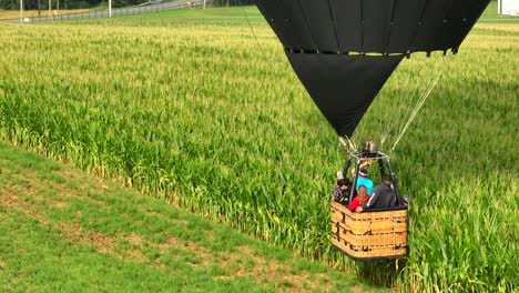 People-Taking-Off-a-Hot-Air-Balloon,-Flying-Very-Close-to-Green-Farm-Fields,-Aerial-Drone-Shot