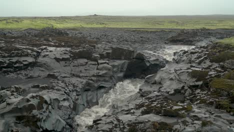 Glacial-River-Flowing-Through-Black-Volcanic-Rock-On-A-Gloomy-Day