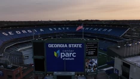 Empty-Center-Parc-Stadium-with-the-American-flag,-home-to-the-Georgia-State-University-Panthers-football-team-at-sunset,-Aerial-Pullback