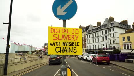 very-visible-yellow-sign-from-protestors-hanging-on-a-light-pole-in-the-middle-of-the-role-with-a-message-about-how-digital-ID-is-a-slavery-with-invisible-chains-by-having-a-chip-inside-our-right-hand