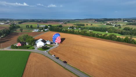 Aerial-birds-eye-shot-of-american-hot-air-balloon-landing-on-wheat-field-in-countryside-area-of-Pennsylvania,-USA