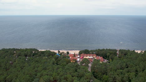 Aerial-establishing-shot-of-Stegna-beach,-view-above-trees,-sandy-strip,-ocean,-and-horizon