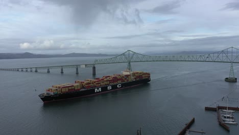 MSC-Cargo-Ship-travels-on-the-Columbia-River-underneath-the-Astoria-Megler-Bridge-In-Astoria-Oregon,-aerial-drone-view