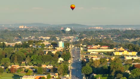 Aerial-wide-shot-showing-road-in-City-with-hot-air-balloon-in-the-air-at-sunset-time,-America