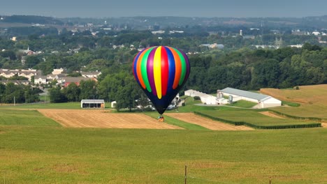 Luftaufnahme-Eines-Bunten-Heißluftballons,-Der-über-Grüne-Felder-Am-Rande-Einer-Amerikanischen-Stadt-Fliegt
