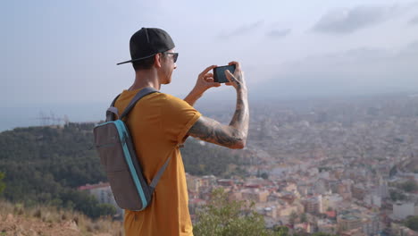 young-men-on-mountain-hike-filming-cityscape-with-smartphone-camera