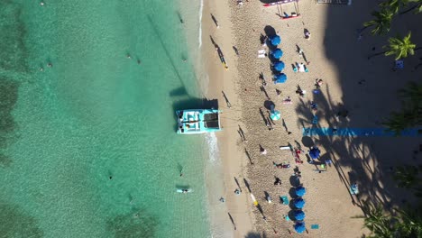 birds-eye-pull-up-shot-of-a-crowded-and-beautiful-clear-green-beach-in-the-meditaranian-ocean-whilst-both-the-locals-and-the-tourists-enjoy-the-weekend-by-the-beach