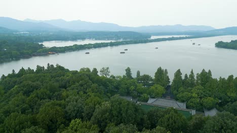 Overcast-Drone-View-of-Hangzhou’s-West-Lake-with-Boats,-Green-Canopy-Below