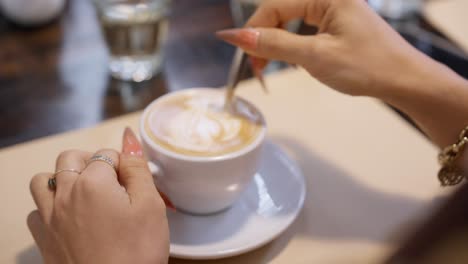 Close-up-of-the-hand-of-a-beautiful-Asian-girl-stirring-suger-a-cup-of-coffee,-preparing-to-enjoy-the-flavor