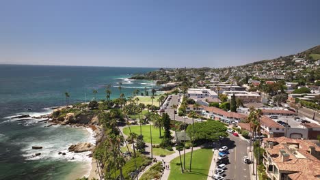 Flying-over-Heisler-Park-in-Laguna-Beach-California-aerial-drone-view-of-the-park,-Pacific-Ocean,-cliffs,-rocks,-palm-trees,-and-big-waves