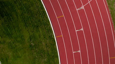 Zoom-out-top-down-aerial-over-the-curve-of-the-100m-finish-line-on-a-track