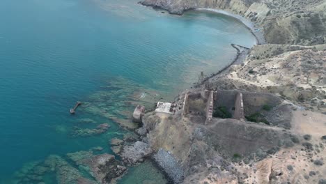 Looking-down-from-above,-we-witness-the-forlorn-remnants-of-an-abandoned-iron-mine-and-a-crumbling-seaside-port