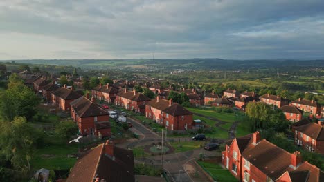 Urban-life-in-the-UK:-Aerial-drone-video-captures-Yorkshire's-red-brick-council-estate-in-the-warm-morning-sun,-featuring-homes-and-people-on-the-streets