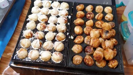 Sizzling-takoyaki-Japanese-octopus-balls,-delicious-golden-brown-street-food-snacks-cooking-on-hot-plate