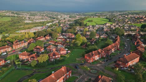City-housing-in-the-UK:-Aerial-drone-footage-of-Yorkshire's-red-brick-council-estate-in-the-warm-morning-sunlight,-featuring-homes-and-vibrant-streets