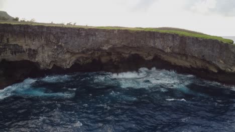 Pan-shot-of-a-cliff-with-waves-crashing-on-rocks,-drone-shot