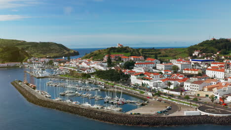 Cinematic-aerial-drone-shot-of-picturesque-local-town-of-Horta-in-Faial-island,-Azores---Portugal-High-view-of-the-ships-docked-at-the-harbor,-green-landscape-in-the-background