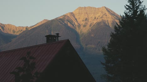 A-charming-house-located-in-the-woods-of-Canada-near-Golden-and-Banff-National-Park,-with-a-huge-mountain-in-the-background,-during-sunrise-hours