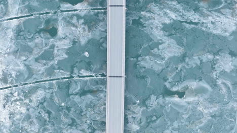 Aerial-view-above-cars-driving-on-a-bridge-at-a-frozen-lake,-winter-day-in-Iceland---top-down,-drone-shot