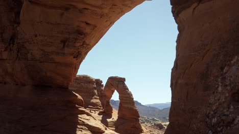 Tilt-up-extreme-wide-shot-of-a-beautiful-natural-red-sandstone-rock-arch-from-a-natural-rock-window