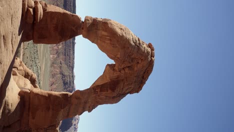 Vertical-handheld-shot-of-a-beautiful-natural-red-sandstone-rock-arch-caused-from-millions-of-years-of-erosion-on-a-hot-sunny-summer-day-in-southern-Utah-on-a-hike-on-vacation