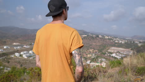 Young-man-with-cap-on-mountain-having-a-glucose-level-sensor-on-tattooed-arm-to-control-diabetics-blood-sugar-level
