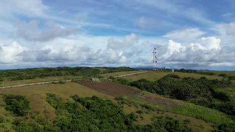 Aerial-view-of-idyllic-farmlands-and-lush-fields-with-satellite-tower-and-stunning-cloudscape-in-background