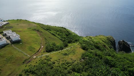 Orbiting-aerial-view-of-cliffside-island-resort-with-lush-greenery-and-turquoise-ocean-bay-in-Catanduanes,-Philippines