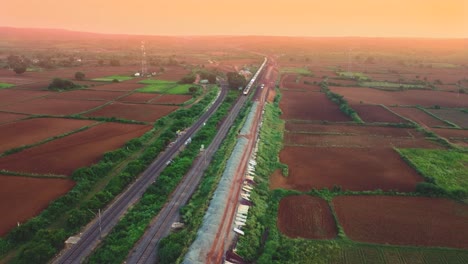 Aerial-drone-shot-of-a-passenger-train-of-Indian-Railways-passing-under-a-Highway-bridge-during-sunset-time-in-Gwalior-India