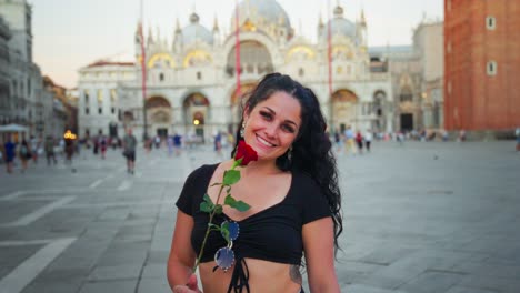 Girl-with-red-rose,-black-shirt,-smiling,-in-city,-tower-in-background,-Venice,-Italy