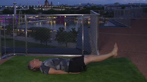 Cool-guy-is-doing-Flutter-Kicks-in-the-evening-on-a-modern-terrace-with-Danube-River-backdrop-in-Vienna,-4K,-Timelapse