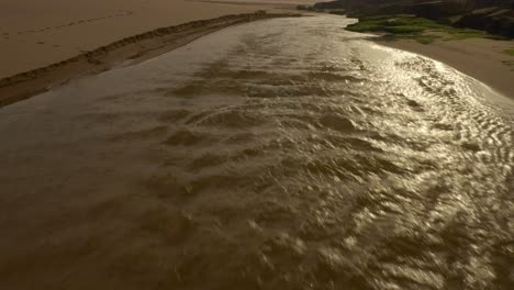 River-Flowing-at-Beach-in-Portugal,-Early-Morning-Golden-Cliffs