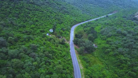 Vista-Aérea-De-Una-Moto-En-Un-Camino-Forestal-A-Través-De-Una-Exuberante-Selva-Verde-Con-Un-Telón-De-Fondo-Montañoso-Durante-El-Monzón-En-Gwalior-Madhya-Pradesh-India