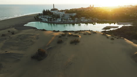 Maspalomas-dunes,-Gran-Canaria:-aerial-view-traveling-out-over-the-dunes-and-spotting-the-Maspalomas-pond-and-the-lighthouse