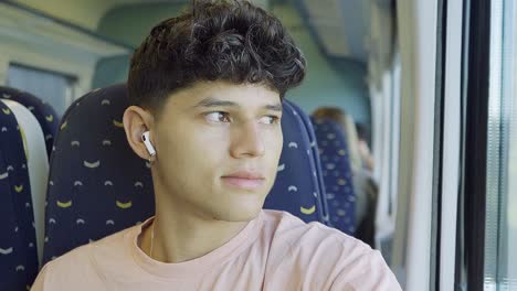 Young-man-traveling-with-the-train-and-listening-to-music-while-looking-outside