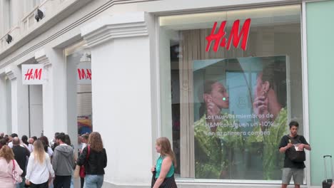Shoppers-walk-past-the-Swedish-multinational-clothing-design-retail-company-Hennes-and-Mauritz,-HandM-store-in-Spain