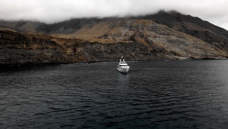 Super-yacht-anchored-outside-a-mystical-island-with-cliffs-in-the-background-and-low-hanging-clouds-with-a-dark-scene
