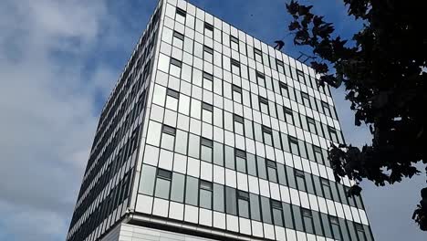 Modernes-College-Bürogebäude-In-Der-Innenstadt-Mit-Glasfront,-Das-Den-Wolkenverhangenen-Blauen-Himmel-Reflektiert,-Langsam-Nach-Unten-Geneigt
