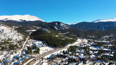 Gorgeous-Breckenridge-Colorado-Mountain-Town-with-Snow-Covered-Houses-and-People-Driving-on-Road-Through-Pine-Tree-Forest,-Aerial-Drone-View