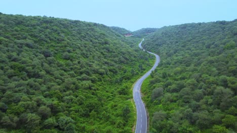 Aerial-Drone-view-of-a-road-through-forest-lush-green-Jungle-with-hilly-backdrop-during-monsoon-in-Gwalior-Madhya-Pradesh-India