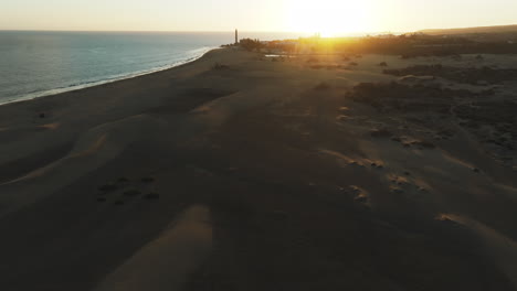 Aerial-view-touring-the-dunes-of-Maspalomas-during-the-sunset-and-seeing-the-shore-of-the-beach