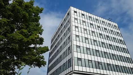 Modernes-College-Bürogebäude-In-Der-Innenstadt-Mit-Glasfront,-Das-Den-Wolkenverhangenen-Blauen-Himmel-Reflektiert,-Schwenk-Nach-Rechts