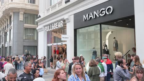 A-crowded-street-with-shoppers-and-pedestrians-walking-past-the-Spanish-multinational-clothing-design-retail-company-by-Inditex,-Pull-and-Bear,-and-Mango-stores-in-Spain